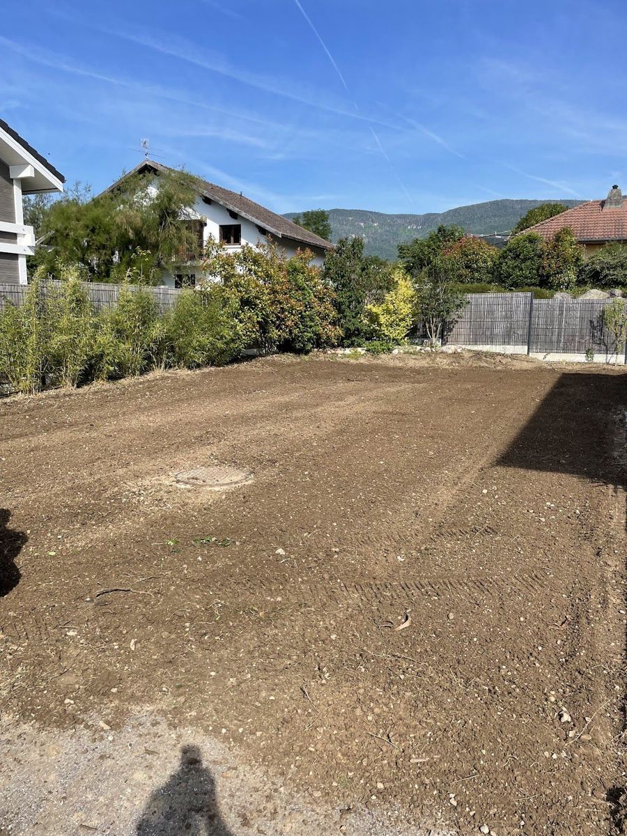 Grand terrain de jardin nivelé et ratissé, prêt à recevoir un gazon, maisons et montagnes au fond